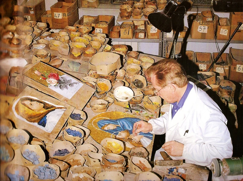 Gino Bonazza al banco di lavoro, tra recipienti di tessere colorate e un mosaico della Madonna